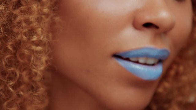 closeup of black womans mouth with bright blue lipstick smiling