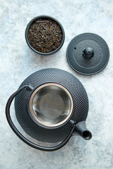 Black metal oriental traditional teapot isolated stone background. Dry tea leafs in small bowl. Top view with copy space.