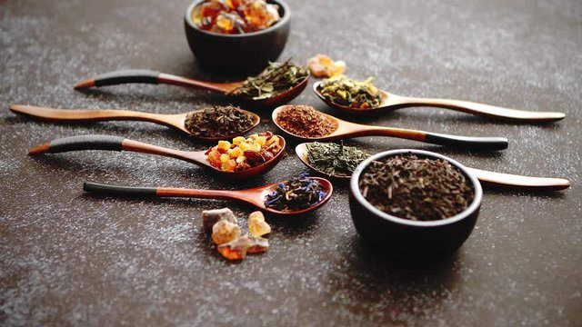 Spoons with different types of dry tea leaves on rusty dark background. Top view.