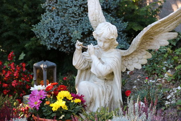 Engel spielt Flöte auf einem Grab mit Blumen im Herbst