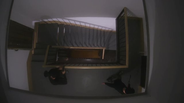 Two bizzare men in black clothes sneaking up on door. Masked men with scrap and gun picking lock. Indoors. Darkness.