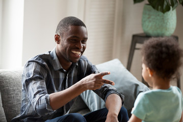 Fototapeta na wymiar Black American father and little preschool son have a fun spend time together weekend sitting on couch at home. African cheerful daddy playing with adorable small child hand game rock paper scissors