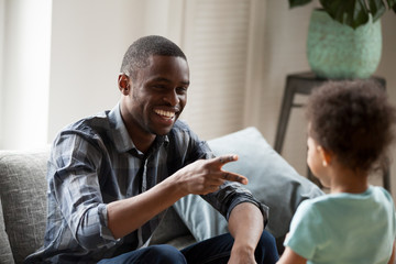 Obraz premium Black American father and little preschool son have a fun spend time together weekend sitting on couch at home. African cheerful daddy playing with adorable small child hand game rock paper scissors