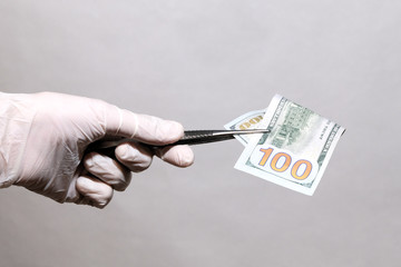 Hand of man hold 100 dollars in the white medical gloves with tweezers.
