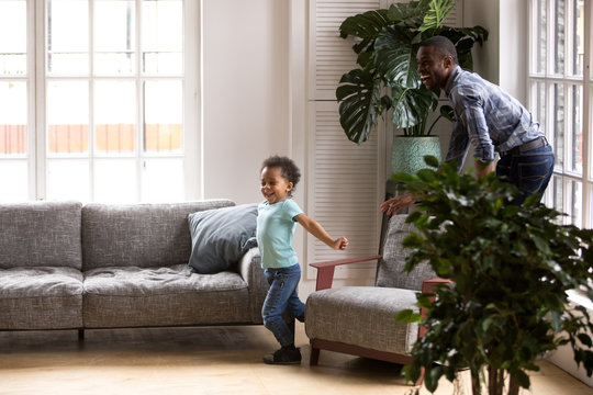 African American family dad and kid have a fun playing tags touch game spend free time on weekend at home. Cheerful father and little preschool toddler son catching each other running in living room
