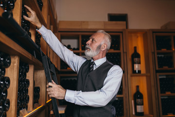 Mature sommelier choosing a bottle of wine at the wine cellar.