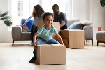 Black married couple sitting on couch in living room unpacking boxes with belongings at new home....