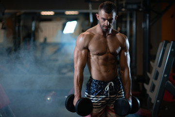 Fototapeta na wymiar young muscular man posing with dumbbells in hand at the gym