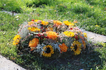 Runder Trauerkranz mit Sonnenblumen und Rosen in Gelb auf dem Friedhof / Gräberfeld