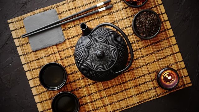 Asian green tea set on bamboo mat with dried green tea. Black vintage iron pot and cups. Asian tea concept