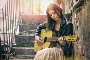 Female musician dressing a leather jacket and a long skirt sitting on antique staircase playing...
