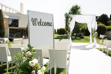 Outdoor wedding ceremony. Welcome plate decorated with fresh flowers on wedding chuppa background