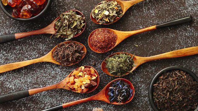 Spoons with different types of dry tea leaves on rusty dark background. Top view.