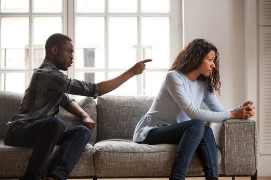 Black married couple sitting on couch in living room at home and quarrelling. Angry husband negative emotionally shouting at wife. Misunderstanding break up problems and trouble in relationship