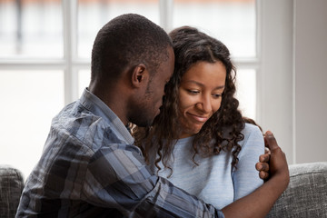 Obraz premium Close up black African married couple in love sitting on couch at home. Loving husband embrace beloved wife after quarrel. Loving boyfriend bored girlfriend. Break up, boredom in relationship concept