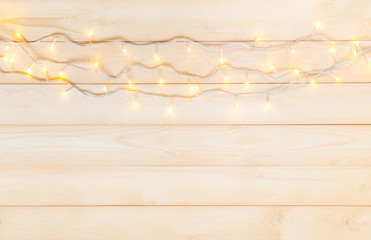 Christmas lights in warm yellow white on string over light wooden background with copy space at the bottom for text, logo decoration on Xmas eve celebration, special holidays, new year event