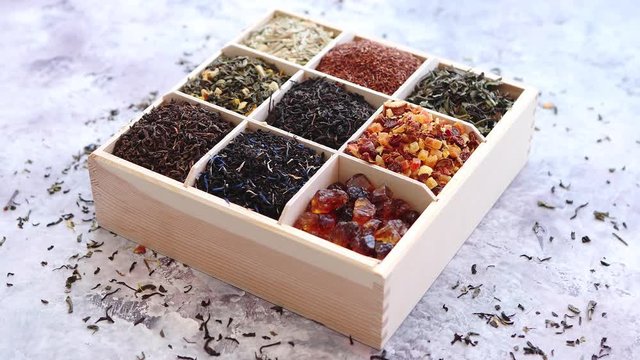 Various kind of dry tea - green, black, red, fruit and blue in wooden box on the table. Top view. Tea time concept.