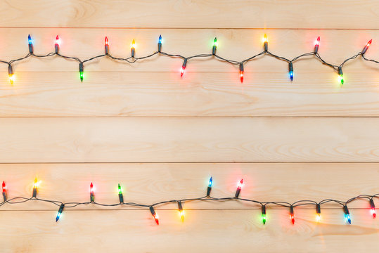 Christmas light bulbs were turned on or lid on string in multi colours; blue, yellow, red, pink, orange and green on light wooden background at night time, Xmas or new year holiday decoration ornament
