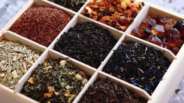 Various kind of dry tea - green, black, red, fruit and blue in wooden box on the table. Top view. Tea time concept.
