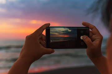 Girl takes pictures on smartphone dawn on the sea