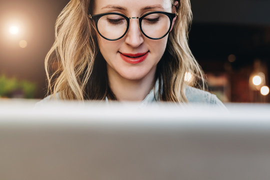 Portrait of young business woman in trendy glasses sitting in cafe,working on laptop.Blogger communicates with followers