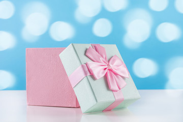 Gently pink baby gift present box with bow on white desk and blue bokeh background. Holiday concept image. Close up, selective focus
