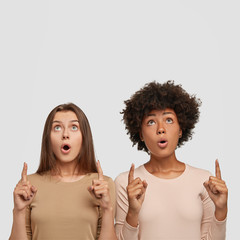Amazed mixed race females has stunning looks, keep jaw dropped, indicate with both index fingers...