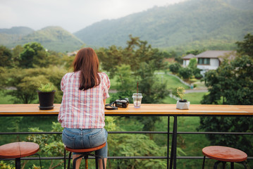 Rear view of young beautiful woman relaxing in the rustic wooden outdoor cafe on mountain.