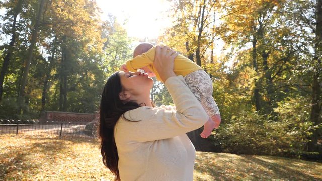 Happy mother tenderly hold and kiss her baby infant daughter in autumn sunny light park