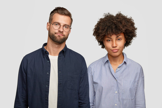 Facial expressions and emotions concept. Horizontal view of puzzled mixed race woman and man have displeased serious looks, have to make project work together, stand closely against white background