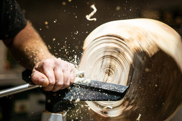 wood working hand edits roating timber with turnery and flying sawdust shavings
