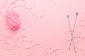 Pink yarn skein, knitting needles and frame of tangled woolen thread on pink table. Top view, hobby or needlework.