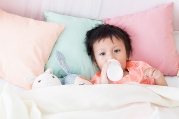 Lovely toddler boy lie down in bed with milk bottle