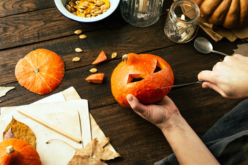 Handing pumpkin with a knife face for a Halloween party, rustic style, wooden background, hands