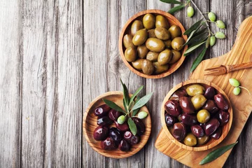 Schilderijen op glas Pickled olives served in bowls from olive wood on rustic kitchen table top view. © juliasudnitskaya