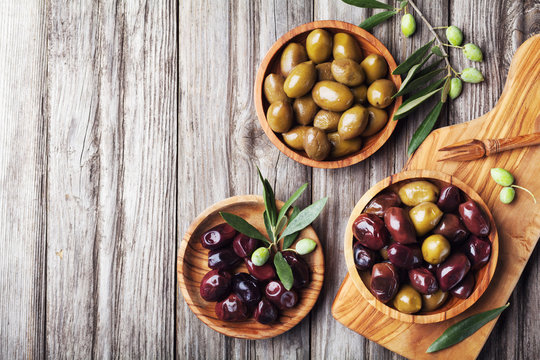 Fototapeta Pickled olives served in bowls from olive wood on rustic kitchen table top view.