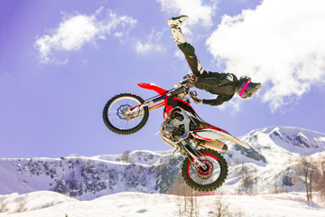 racer on a motorcycle in flight, jumps and takes off on a springboard against the snowy mountains