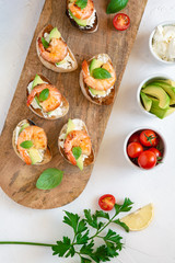 Bruschetta italian snack sandwiches with shrimps, avocado and cheese decorated by basil.