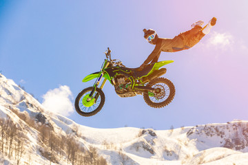 racer on a motorcycle in flight, jumps and takes off on a springboard against the snowy mountains