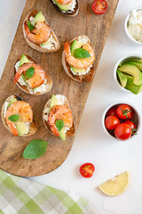 Bruschetta italian snack sandwiches with shrimps, avocado and cheese decorated by basil.
