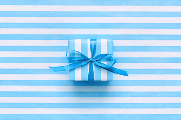 Festive gift box on blue and white striped wrapping paper. Minimal pastel background with space....