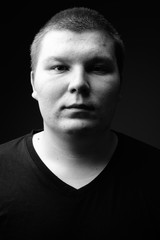 Overweight young man against black background in black and white