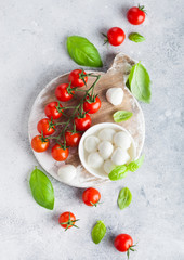 Naklejka na ściany i meble Fresh Mini Mozzarella cheese on vintage chopping board with tomatoes and basil leaf on stone kitchen table background.
