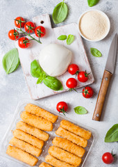 Fresh Mozzarella cheese on vintage chopping board with tomatoes and basil leaf and tray with cheese sticks on stone kitchen table background.