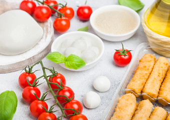 Fresh Mozzarella cheese on vintage chopping board with tomatoes and basil leaf with olive oil and tray with cheese sticks on stone kitchen table background.