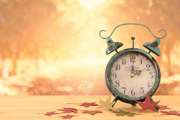 Image of autumn Time Change. Fall back concept. Dry leaves and vintage alarm Clock on rustic wooden...
