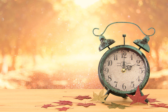Image of autumn Time Change. Fall back concept. Dry leaves and vintage alarm Clock on rustic wooden table.