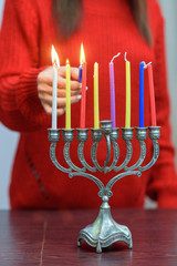 Fototapeta premium Jewish Woman lighting Hanukkah Candles in a menorah. People celebrate Chanukah by lighting candles on a menorah, also called a Hanukiyah. Each night, one more candle is lit.