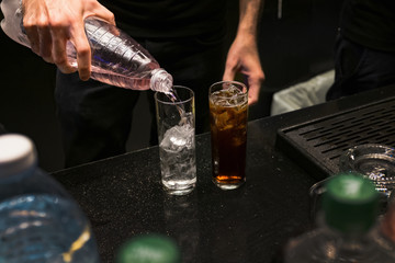Bartender is creating cocktails in bar or at night club He is holding two bottleы. The man is pouring beverage from it into two glasses. Expert barman