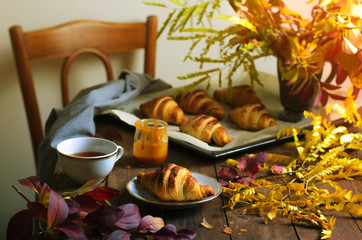 Cozy Autumn Still Life, Freshly Baked Croissants with Cinnamon and Salted Caramel, Cup of Tea and Fall Leaves on Wooden Table
